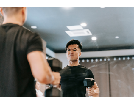 fit healthy asian man wearing a black exercise t-shirt doing bicep curls with a dumbbell at his home gym
