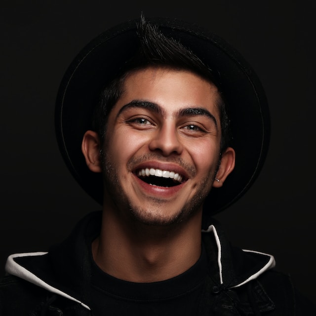 young man with black hair and black shirt with black background smiling
