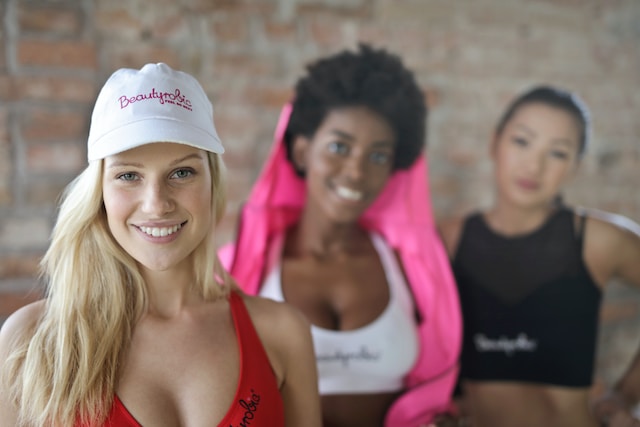three young fit and healthy wearing sports bras with one wearing a white hat smiling 