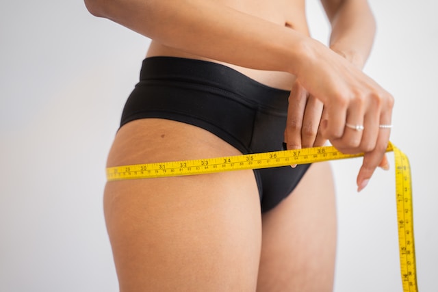 woman wearing black underwear measuring her hips with a tape measure