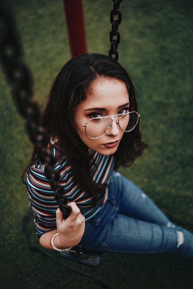 woman with brown hair and glasses on sitting on a swing