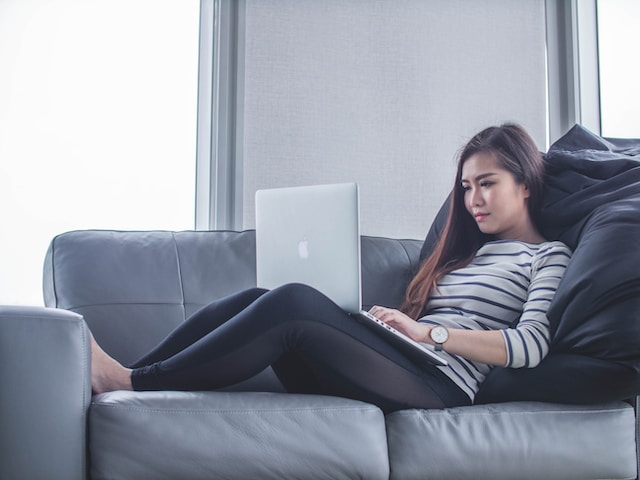 asian woman wearing black leggings and striped sweatshirt sitting on the couch doing her online fitness assessment on her lap at her home
