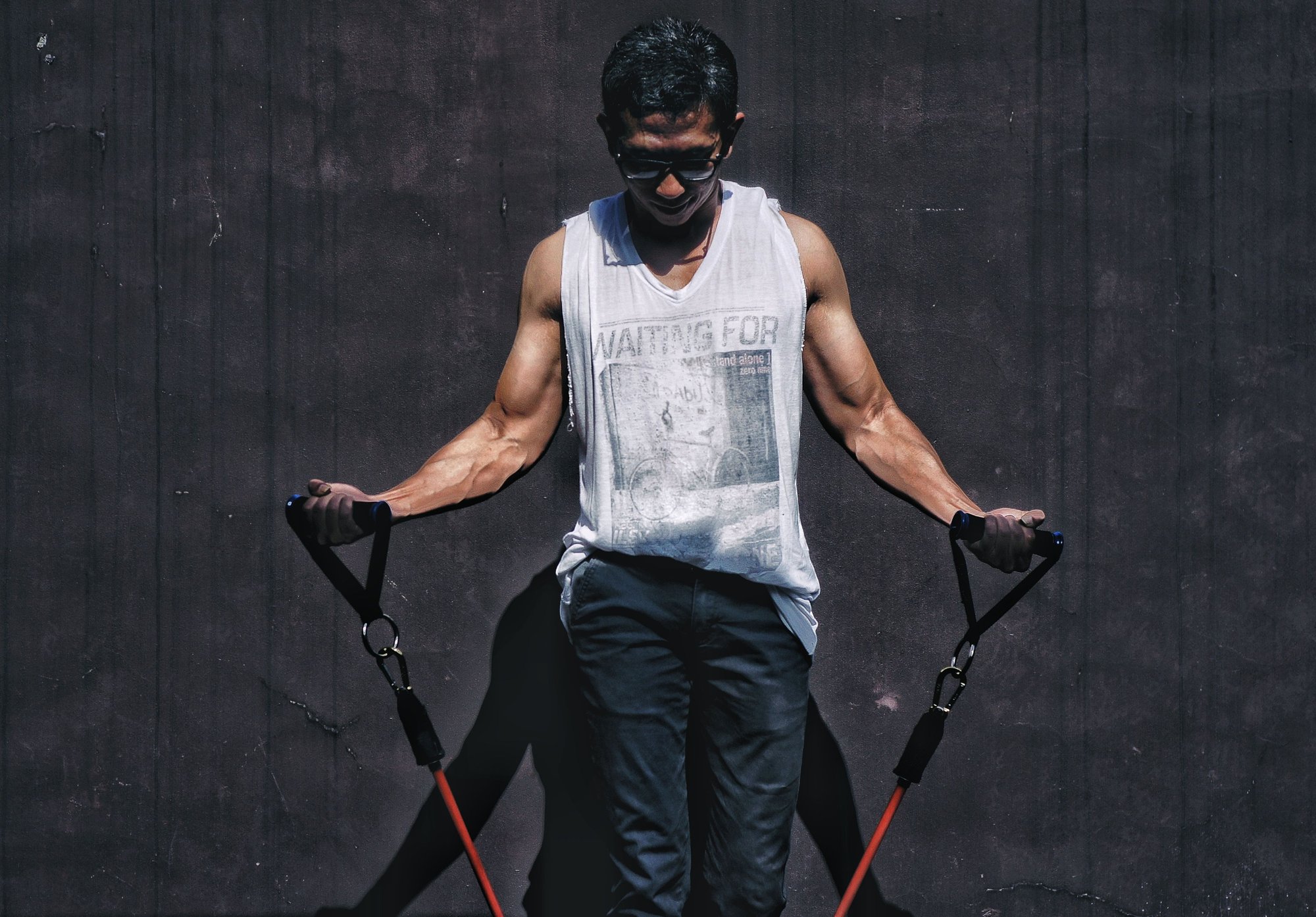 fit healthy latin man with cut-off t-shirt and black pants doing bicep curls with resistance bands