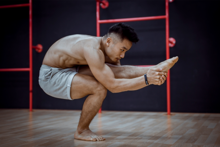 fit strong muscular asian man with grey shorts and no t-shirt holding one of his legs while doing a one-legged squat