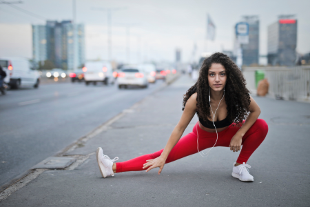 fit healthy latin woman in red exercise leggings and black sports bra with beautiful curly hair stretching her legs out after a sweaty run