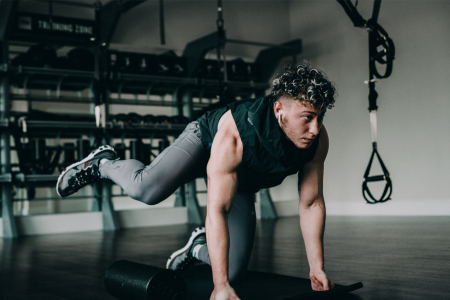 latin man with grey sport pants and black cut-off shirt doing leg exercises at a gym