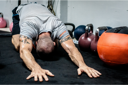 strong athletic man wearing a grey exercise t-shirt stretching his lower back on a black mat surrounded by kettlebells 