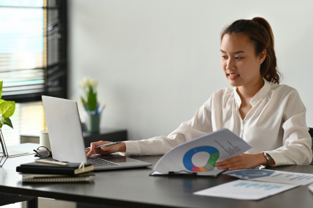 fit healthy asian woman checking her laptop at work while holding a graph about nutrition details from her client