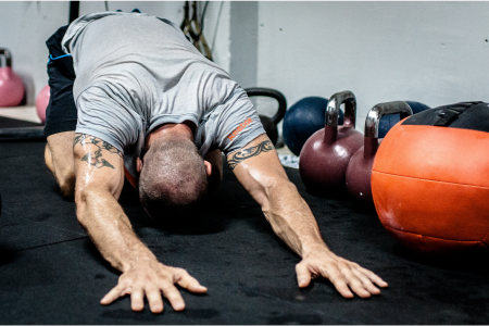 fit athletic muscular man wearing a grey exercise t-shirt and black shorts stretching his lower back at a gym